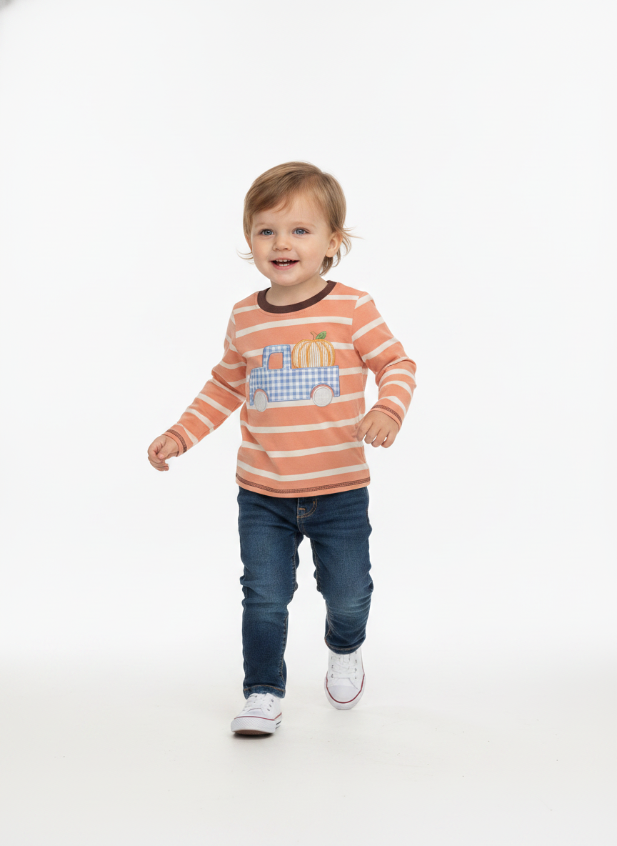 A toddler boy walking forward on a seamless white studio background, wearing a long-sleeve orange and white striped shirt with a blue gingham truck graphic on the chest, paired with dark blue jeans and white sneakers.