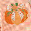 A close-up of an embroidered pumpkin applique with a large floral bow, green stem, and orange leaves, stitched onto an orange and white gingham fabric background.
