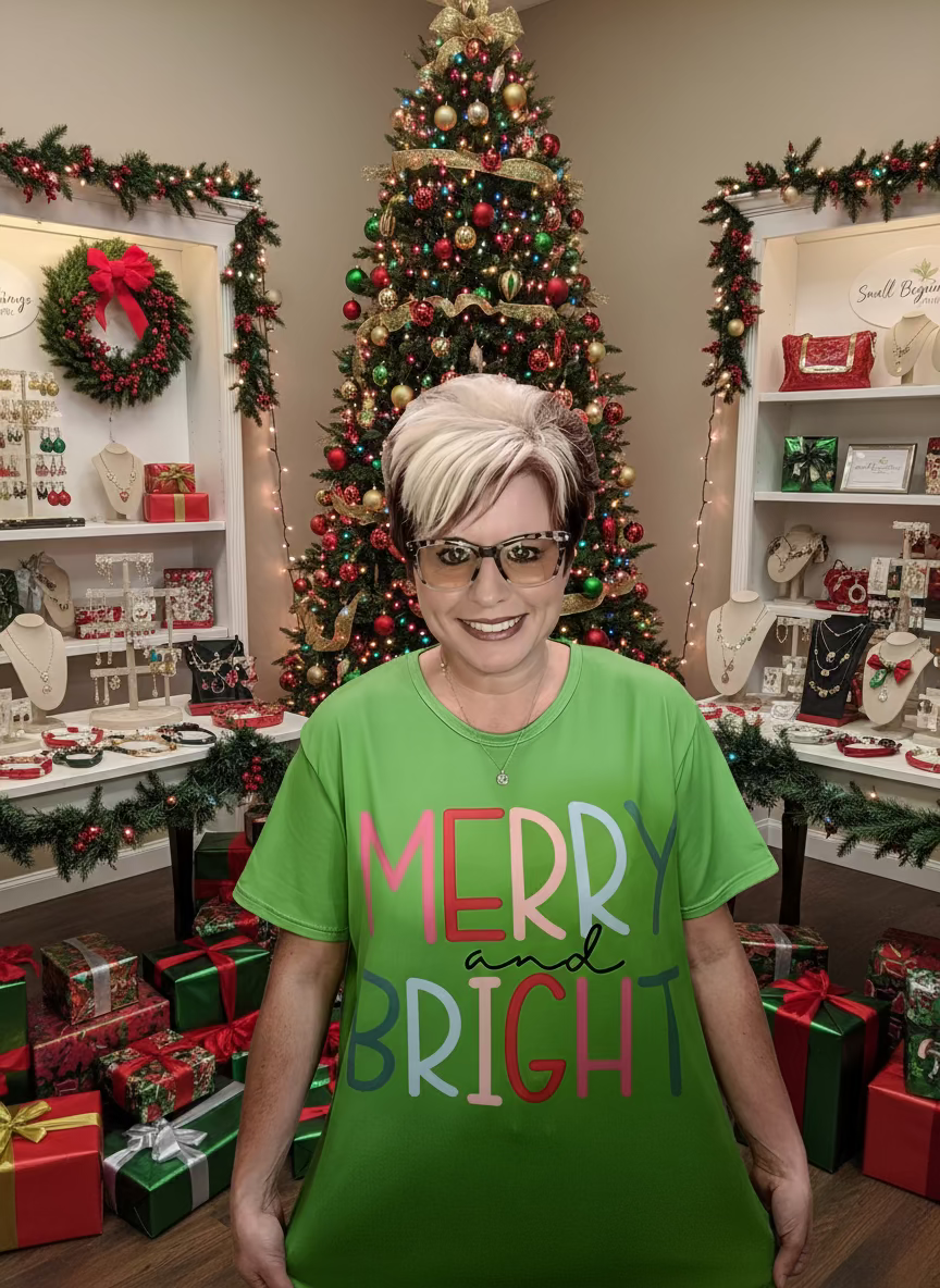 Person wearing a green shirt with 'Merry and Bright' text in front of a wooden wall with 'Small Beginnings Boutique' sign.