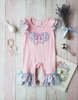 Pink baby romper with 'Good is good' text on a wooden surface with decorative items.