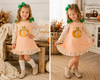 A toddler girl modeling a long-sleeve gingham dress in a split-screen lifestyle photo. The dress has a pumpkin graphic on the front, floral ruffle trim, and green bow hair clips.